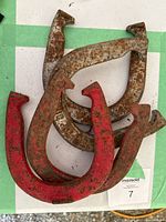 Four rusted metal horseshoes stacked showing varying amounts of red paint residue and rust.