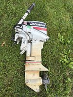 Full side view of motor on grass showing tiller handle, housing and prop