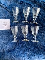 Set of 6 crystal liquor glasses arranged in two rows of three on a blue textured fabric background, showing clear pinwheel pattern on each glass bowl with a short stem and flat base.