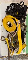 Multiple ratchet straps in yellow, black, and green colors with metal hooks and ratchets, showing rust and wear, laid out on a table.