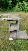 Side view of the gray metal rolling cart on grass showing three shelves and two wheels