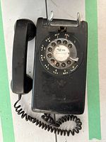 Top view of black rotary phone showing rotary dial with number and letter markings and handset connected by coiled cord.