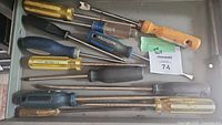 Nine assorted screwdrivers laid out inside a drawer, varying handle colors and types visible.