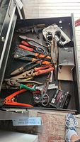 Drawer with various hand tools including scissors, shears, nailer stapler, wire cutters, and drill bits in boxes