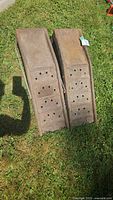 Pair of metal tire ramps displayed on grass showing top view with holes and rust spots.