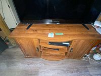 Front view of wooden TV stand with TV on top, shows wood finish and scratches