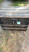 Closed view of rectangular wooden chest with metal reinforcements and metal handles on sides.