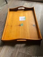 Top angled view showing the natural wood grain, curved handles, and minor surface marks on the wooden tray.