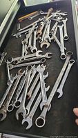 Photo shows a collection of about 30 combination wrenches in various sizes scattered on a black tray. Some wrenches show rust and dirt.