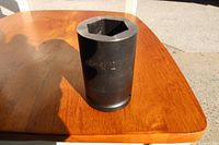 Photo showing the impact deep socket with 1-1/2 inch marking on its side, placed on a wooden surface with natural light casting shadows.