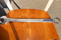 Photo showing a 1-1/2 inch Truecraft combination wrench placed on a wooden surface outdoors in sunlight. The wrench features an open-end and a 12-point box-end, stamped with size and brand.