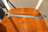 Full view of a 1-1/4 inch Truecraft combination wrench placed on a wooden surface in sunlight, showing both open-end and box-end sides with visible branding and size markings.