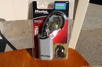 Two identical Master MiniSafe combination locks in original packaging placed on outdoor surface. Packaging indicates free MiniSafe and shows combination padlock with cable.