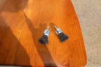 Two wire brush wheels on a wooden surface photographed from above with sunlight shadow.