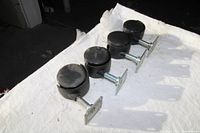 Four black swivel caster wheels laid out on a white fabric surface, shows top and side views.