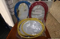 Photo of three refrigerant charging hoses in blue, red, and yellow colors, each 72 inches long, packaged in plastic bags, arranged against a wall corner.