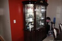Wooden china cabinet with glass front doors and lights inside shown against a wall in a room with chairs nearby