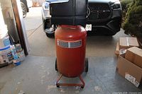 Front view of red vertical air compressor tank with black compressor head and wheels.