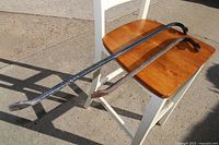 Two crowbars laid on a wooden chair, one longer black-finished crowbar and one shorter rusted crowbar.