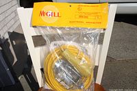 Photo of original packaged McGill heavy duty drop light showing yellow coiled cord, protective cage, and yellow plug