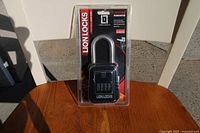 Photo showing a new black LIONLOCKS Portable Lock Box with a 4-digit combination lock in original packaging on a wooden table.