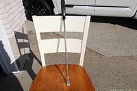 Pry bar placed on wooden chair showing full length including the black plastic handle and metal shaft with tapered pry end.