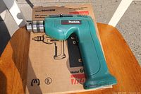 Makita cordless drill resting on its original box, showing the drill from left side with Makita label and metal chuck visible.
