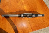 Photo showing metal reaming tool with threaded end and middle adjustable blade section placed on wooden surface in sunlight