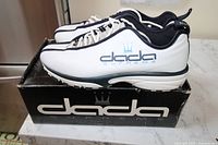 Side view of white and blue Dada Supreme sneakers on top of original black branded box showing logo details and condition