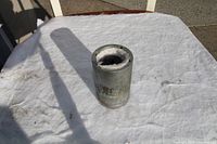Large metal deep socket tool placed on a white cloth surface outdoors, showing cylindrical shape and socket opening on top.