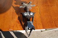 Photo of metal valve spring compressor tool featuring a star-shaped adjustment knob, spring, and clamp on a wooden surface.