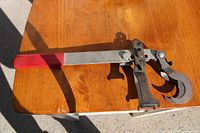 Valve spring tool showing metal lever clamp and red grip handle lying on wooden surface.