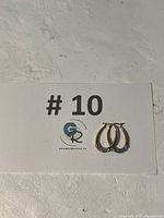 Pair of oval-shaped two-tone 10k gold hoop earrings placed on a white card with the number 10 printed on it.