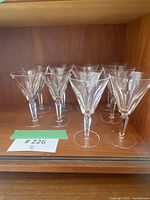 Front view of 10 crystal wine glasses arranged in two rows on wooden shelf.