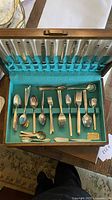 Full view of flatware set inside the anti-tarnish storage box. The box interior is lined with turquoise felt and cream fabric. The set shows a variety of spoons, forks, and serving utensils separated and secured in place.