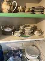 Full set displayed on two kitchen shelves, cups stacked with saucers, teapot, creamer and sugar bowl visible