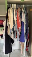 Closet rod with assorted women's tops and blouses on hangers in various colors and patterns.