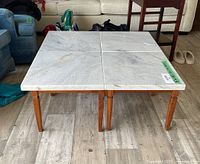 Four marble topped tables seen assembled side by side on a wooden floor with surrounding living room furniture.