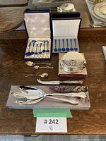 Overall lot view: two fitted cases of blue enamel spoons, loose camel spoon, silver-plated servers in box.