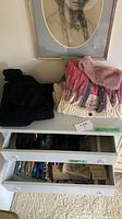 Drawers containing various scarves and accessories, with two knit sweaters on top of the dresser.