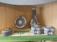 Group photo of 5 Wedgwood blue jasperware pieces including vase, plate, and three covered boxes with white classical relief.