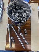 Top view showing the can filled with various sized 1/4 inch drive sockets, with the ratchet, extensions, and socket adapters arranged outside the can on a wooden surface.