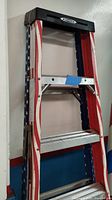 Side view of 6 ft aluminum step ladder showing American flag design on rails and three steps.