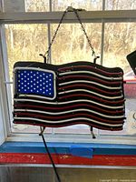 Photo of the American flag neon light hanging in a window, displaying the blue star section and red and white stripes in neon tubing.