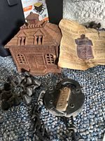 Cast iron house-shaped bank, vintage Albany padlock with chain, decorative cast iron piece, and partial view of newspaper inset.