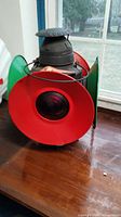 Front and side view of antique railroad light showing the large red lens and metal structure on a wooden table.