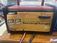 Front view of battery charger showing brand, model, and charge settings with attached cables and clips.