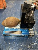 Sony Blu-ray player in original box, Wilson football on top, vintage plasma ball with power adapter on side, shown on floor surface.