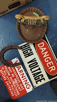 Cast iron ashtray, horseshoe, Danger High Voltage sign, and Warning Dangerous Gas sign on blue floor