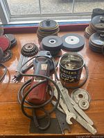 Top view of assorted polishing wheels, cutting wheels, wire brushes, grinding wheel, the Hilti grinder, metal wrenches, and a can containing additional accessories.